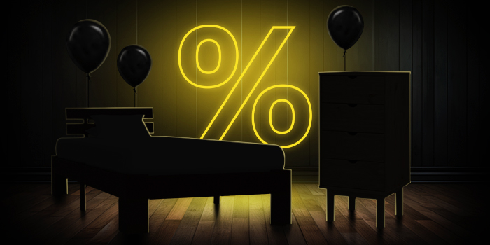 Melna gulta un kumode ar melniem baloniem spoži dzeltenas procentu zīmes priekšā uz tumšas koka grīdas.